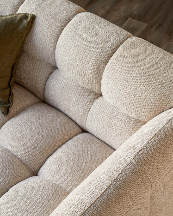 A close up of a comfy, cream coloured, cushioned sofa, with a green cushion on one corner.