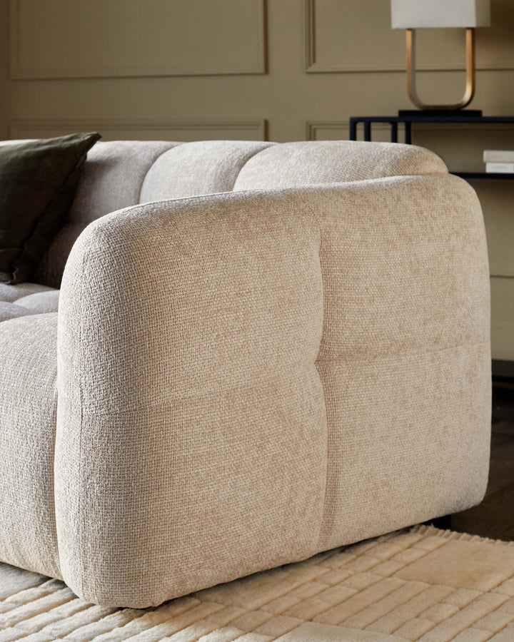 Close-up of a cream, textured sofa with a dark green cushion and a black side table with a lamp.