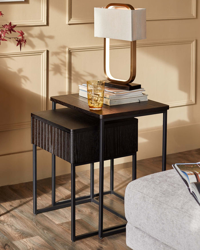 Nesting tables in dark wood with a lamp and books on top, beside a grey sofa.