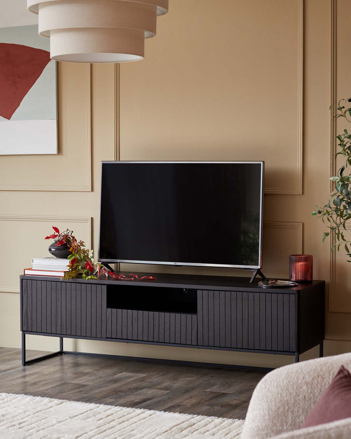 A dark wood TV stand with grooved doors, supporting a flatscreen TV. Accessories include a vase, books and candle.
