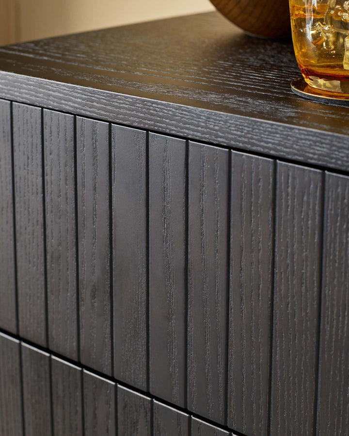 Close-up of a modern black wood cabinet with reeded drawer fronts, showcasing its texture and design.