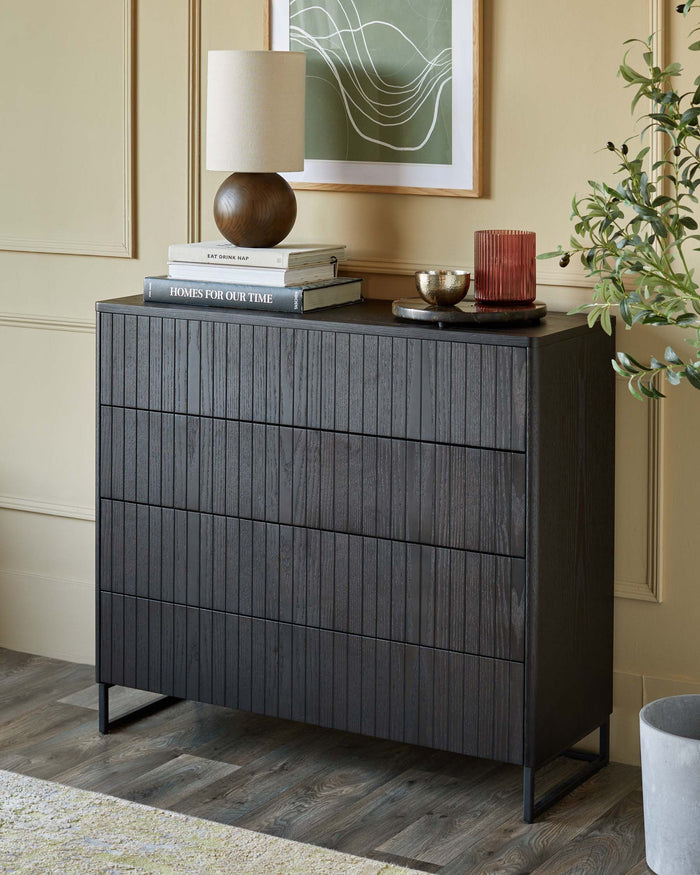 A three-drawer chest of drawers in a dark wood finish, with a lamp and books on top.