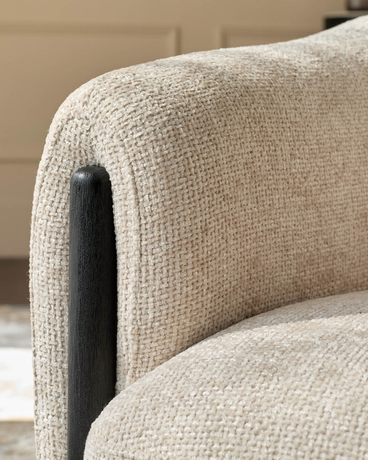 Close-up of an armchair with textured cream upholstery and dark wooden armrest. Minimalist design.