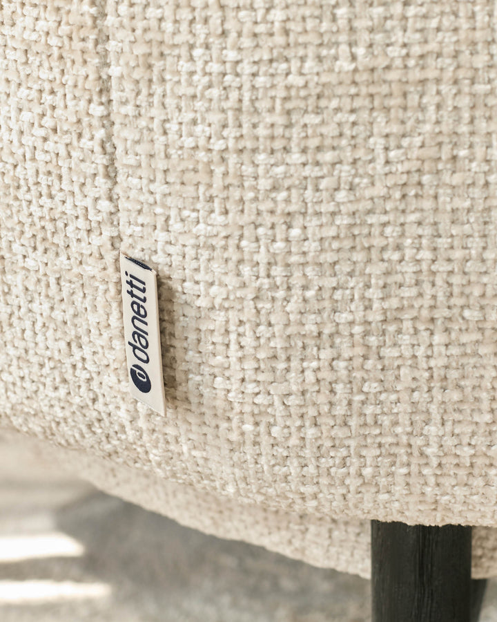 Close-up of a textured, neutral-toned armchair with a discreet 'Danetti' label, highlighting its quality craftsmanship.