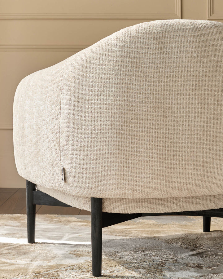 Close-up of a light-beige armchair with dark wood legs, showcasing its textured fabric and modern design.