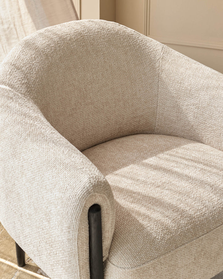 Close-up of a stylish beige armchair with dark wood legs and textured fabric.