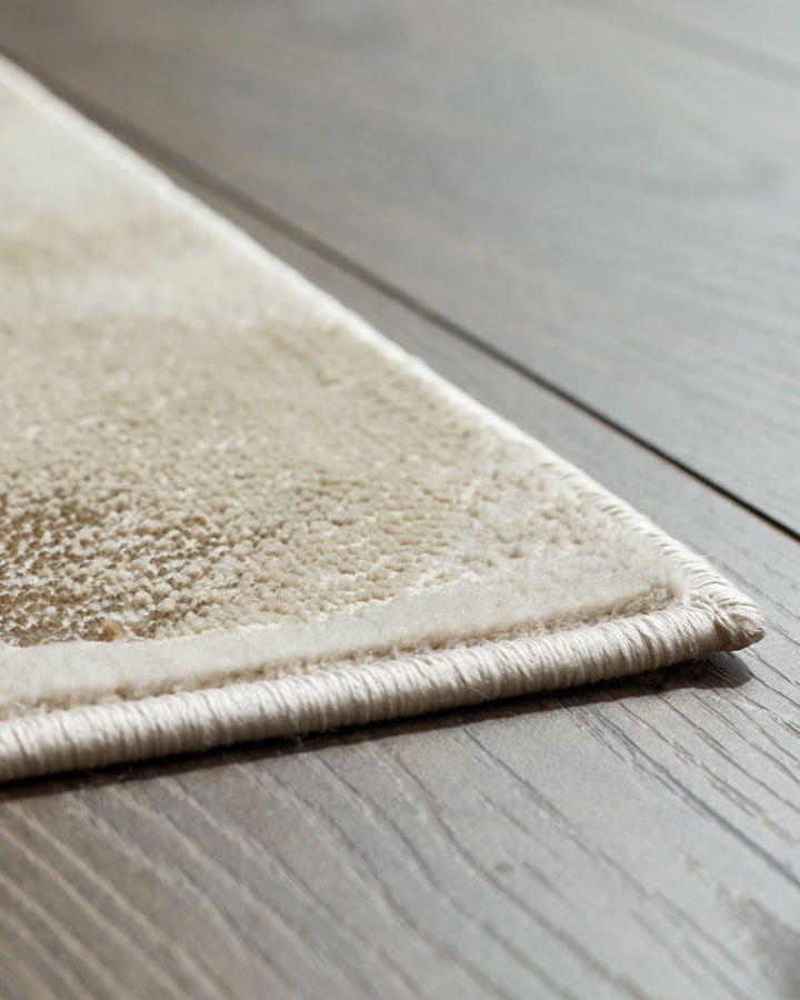 Close-up of a cream rug with textured detail and bound edge, set against a dark wood floor.