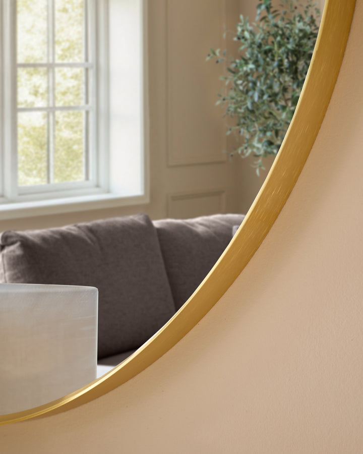 Large round gold-framed mirror with curved edge detail, displayed in a modern living room setting.