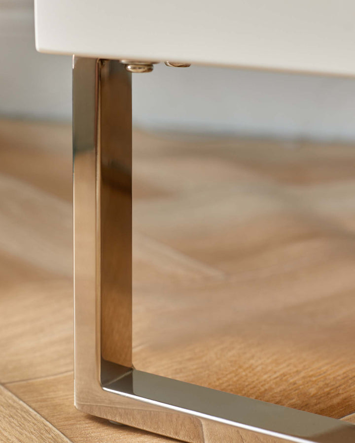 Close up of a sleek, modern table leg made of chrome on a wooden floor.