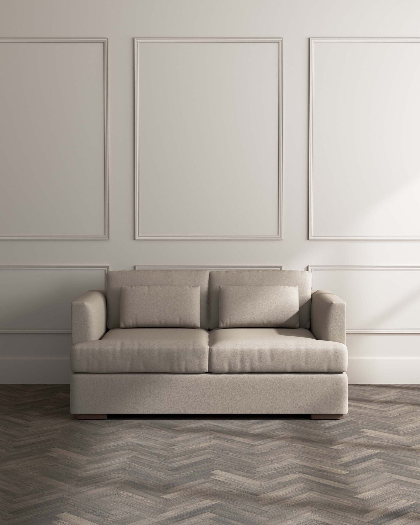 Modern minimalist beige upholstered sofa with clean lines and rectangular cushions on a herringbone parquet floor against a light grey wall with framed artwork.