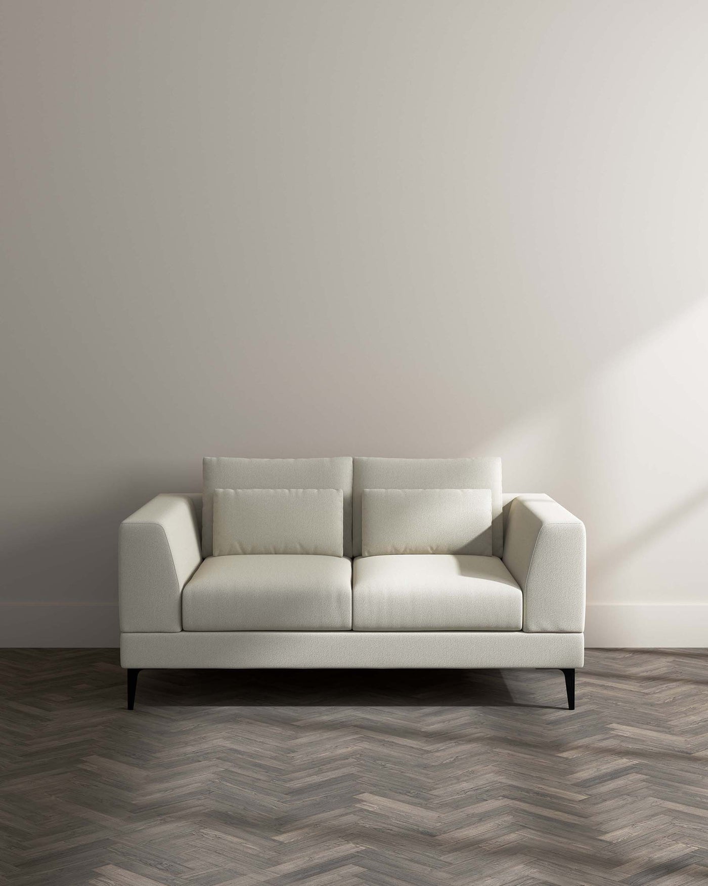 Modern light-coloured fabric sofa with clean lines, featuring plush back cushions and a tailored silhouette, set against a neutral wall on a herringbone-patterned wood floor.