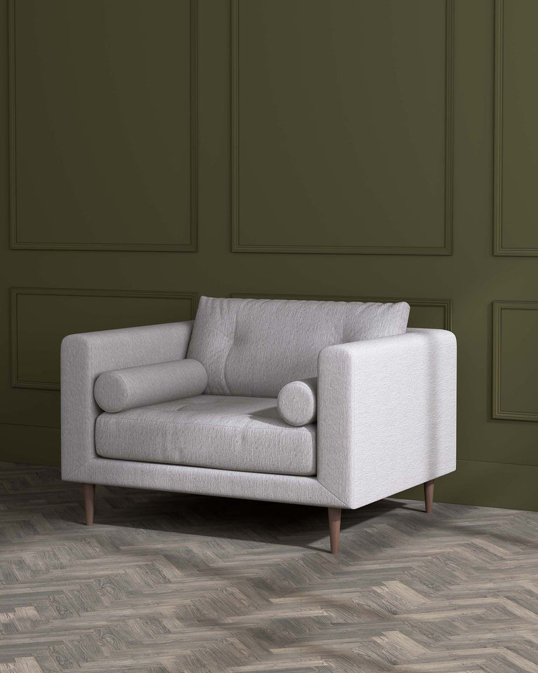 A modern, minimalist two-seater sofa with a textured light grey fabric upholstery and clean, straight lines. The sofa features one seat cushion, a broad backrest, a cylindrical bolster pillow, and two squared armrests, all supported by four angled wooden legs. The sofa is set against a monochromatic green painted wall with traditional panel details and rests on a herringbone-patterned wooden floor.