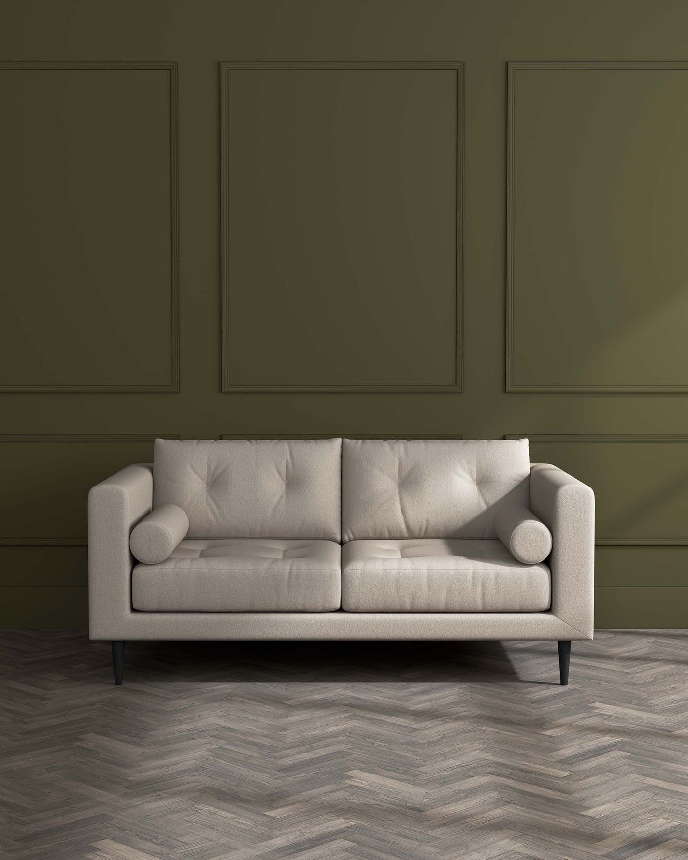 A modern three-seater sofa in a light beige fabric with tufted backrest, clean lines, cylindrical armrest cushions, and tapered black legs, set against a dark olive green wall with decorative moulding and herringbone-patterned wooden flooring.