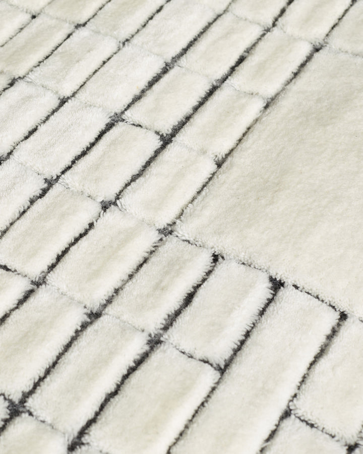 Close-up of mosaic large sculpted wool rug in monochrome, showing textured rectangular blocks in cream and charcoal.
