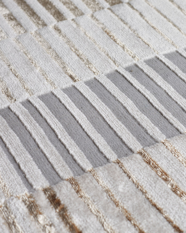 Close-up of textured rug showing cream and gray striped pattern with metallic thread details.