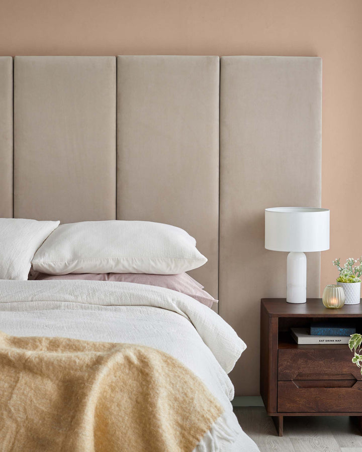 A modern bedroom featuring a plush taupe headboard, cozy bedding, a stylish wooden bedside table, and a chic lamp.