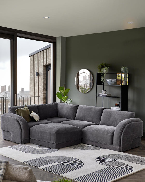 A spacious gray sectional sofa with curved arms, complemented by a patterned rug and minimalist black shelving unit.