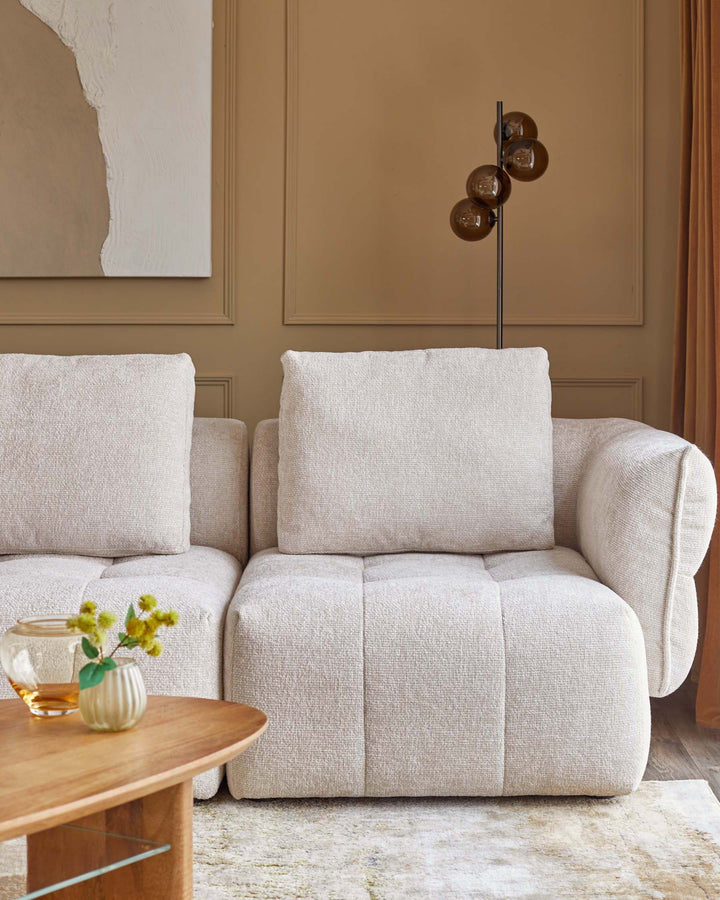 A cozy beige sectional sofa with plush cushions, accompanied by a round wooden coffee table and a sleek floor lamp.