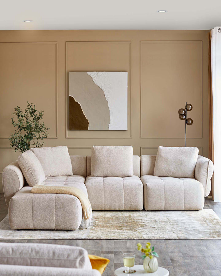 Contemporary light beige sectional sofa with plush cushions, accompanied by a decorative throw and a round side table.