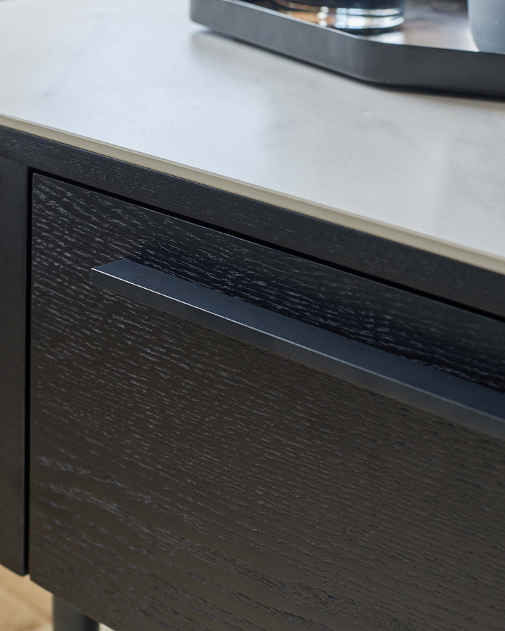 Close-up of a black, wood-grain drawer with a sleek, metal handle, set beneath a light, marble-effect top surface.