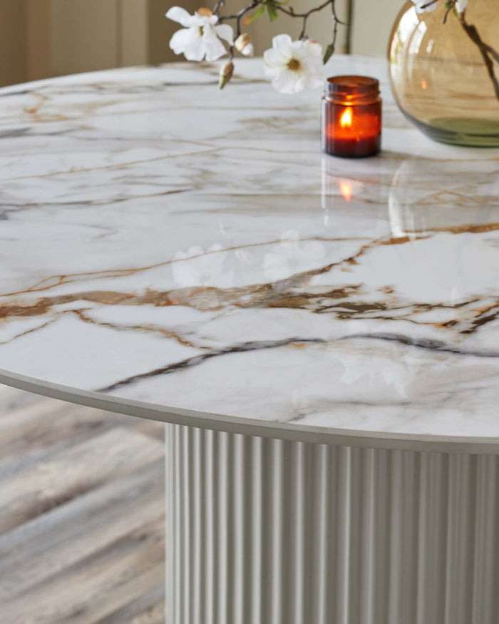 A round table with a marble effect top and a fluted pedestal base, illuminated by a candle and accented with flowers.