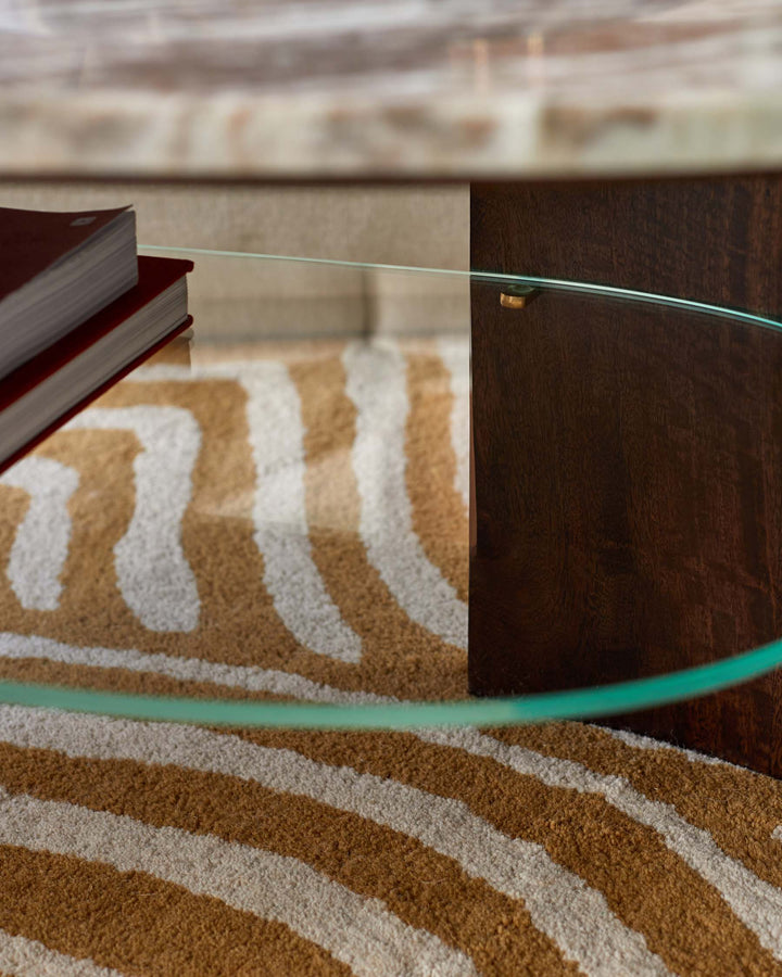 A modern coffee table with a marble top, glass shelf and a dark wood leg, sitting on a zebra print rug.