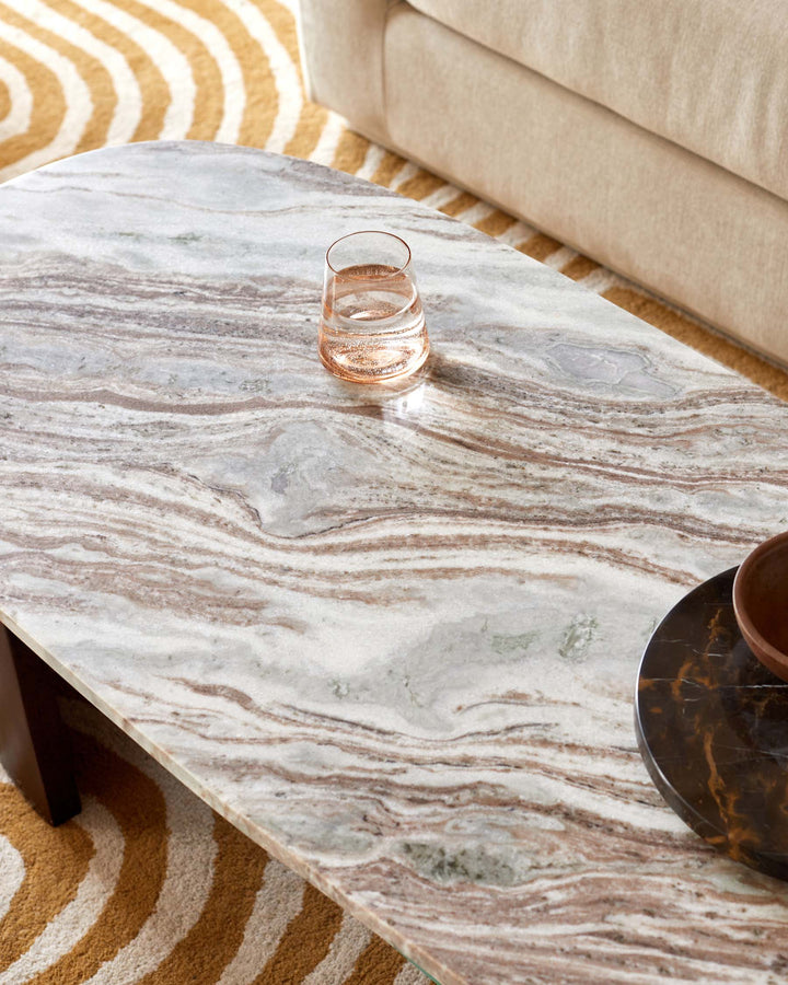 A marble table hosts a glass of water and a bowl, all set against a patterned rug and beige sofa.