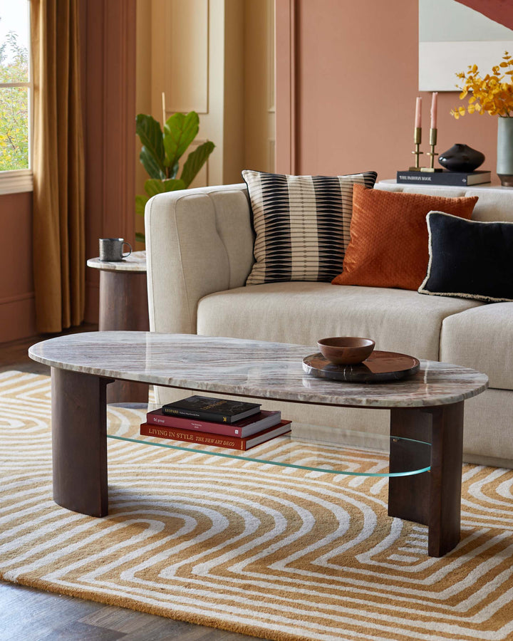 A stylish living room featuring a marble coffee table, neutral sofa with cushions and a patterned rug, creating a cosy interior design.