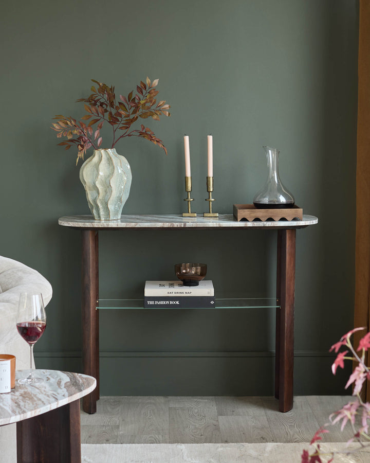 Adalynn console table in dark wood with white marble top, displayed in styled interior setting with decorative items.