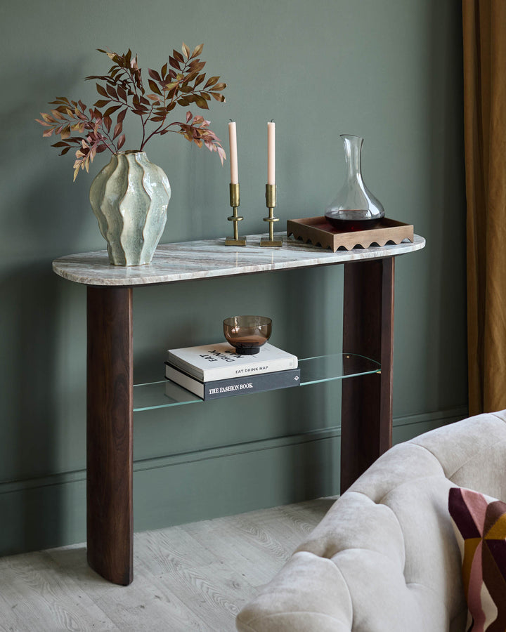 Adalynn console table in dark wood with white marble top and glass shelf, styled with decor in modern bedroom setting.