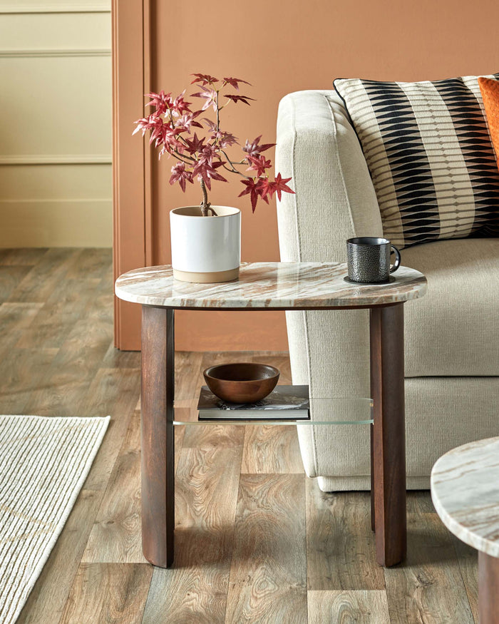 Oval side table with marble top, wood legs, glass shelf, styled with plant, bowl and mug.