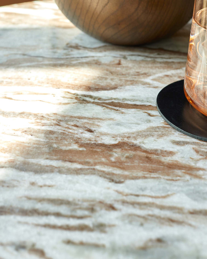 Close-up of a marble table top, featuring a wooden bowl, a glass, and a black coaster. A modern and stylish furniture detail.