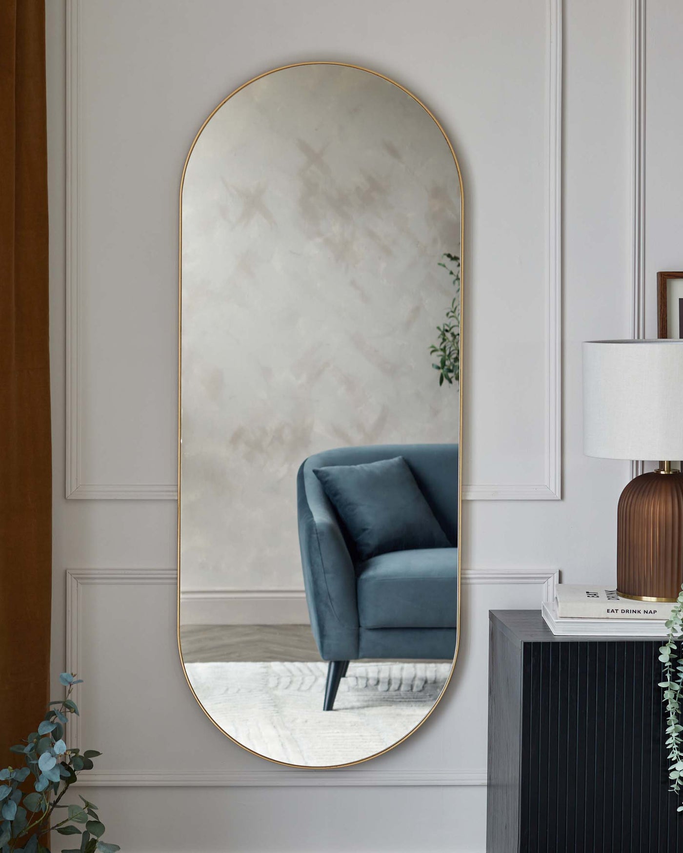 Elegant modern furniture in a chic interior, featuring a sleek, black wood cabinet with vertical grooves and a plush blue velvet armchair with a high back and angled metal legs, complemented by a tall, arched floor mirror with a slim gold frame.