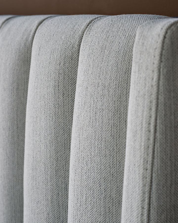 Ivory fabric bed with vertical channel quilting detail, close-up showing textured upholstery and plush stitched design.