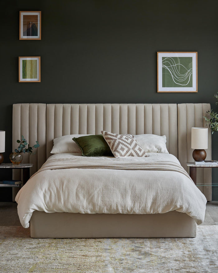 Bedroom with beige bed, upholstered headboard, side tables with lamps, and abstract art on a dark green wall.