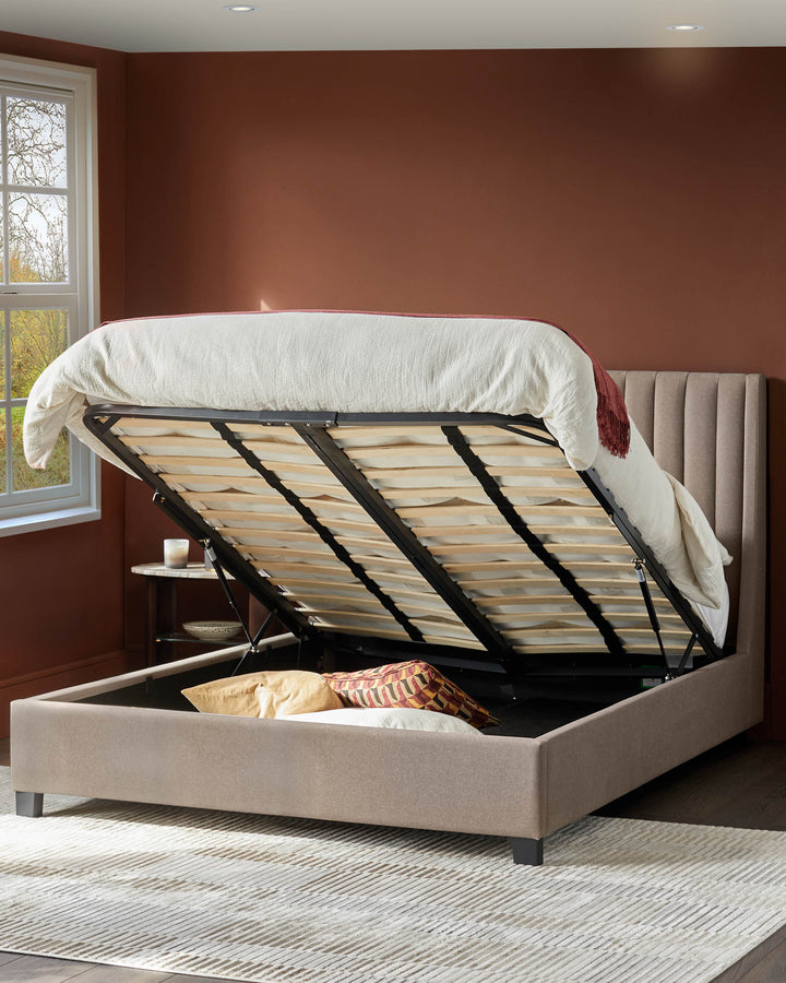 Upholstered bed with slats revealed, storage space underneath. Neutral rug and warm brown walls, with a side table.