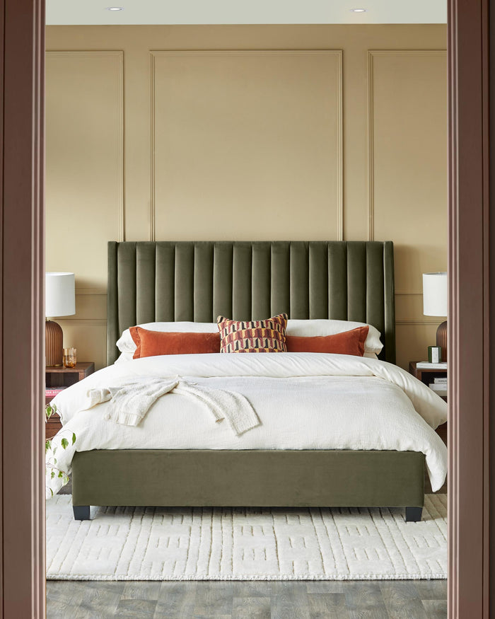 Bedroom with a green velvet bed, bedside tables with lamps and a cream rug in a beige room.