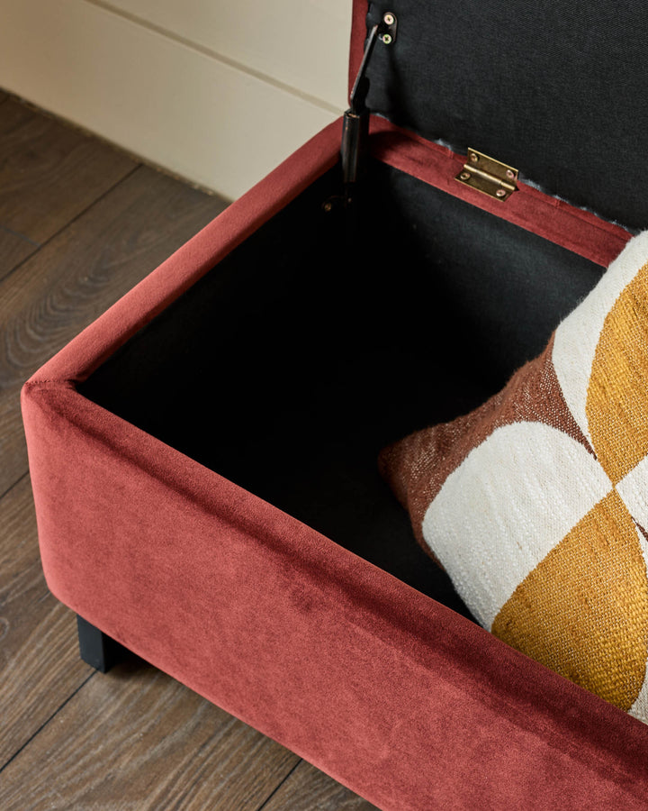Amalfi velvet ottoman bench in toffee red with open storage compartment, showing black interior and brass hardware detail.