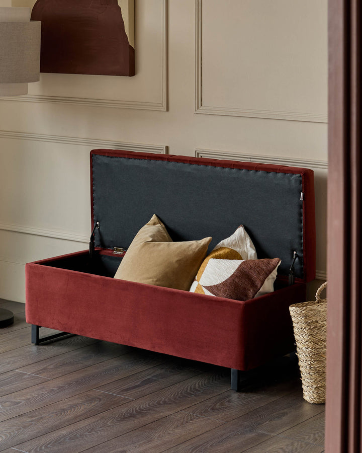 Red velvet ottoman bench with open storage lid, displaying decorative pillows inside and dark interior lining.