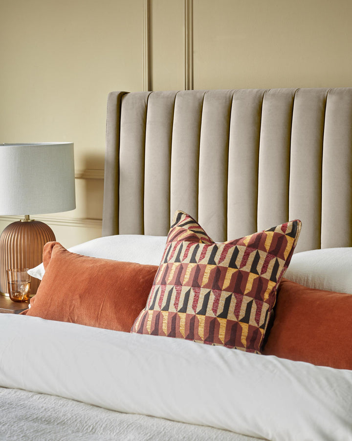 Bedroom featuring a headboard, bedside table with lamp and an arrangement of cushions on a white bed.
