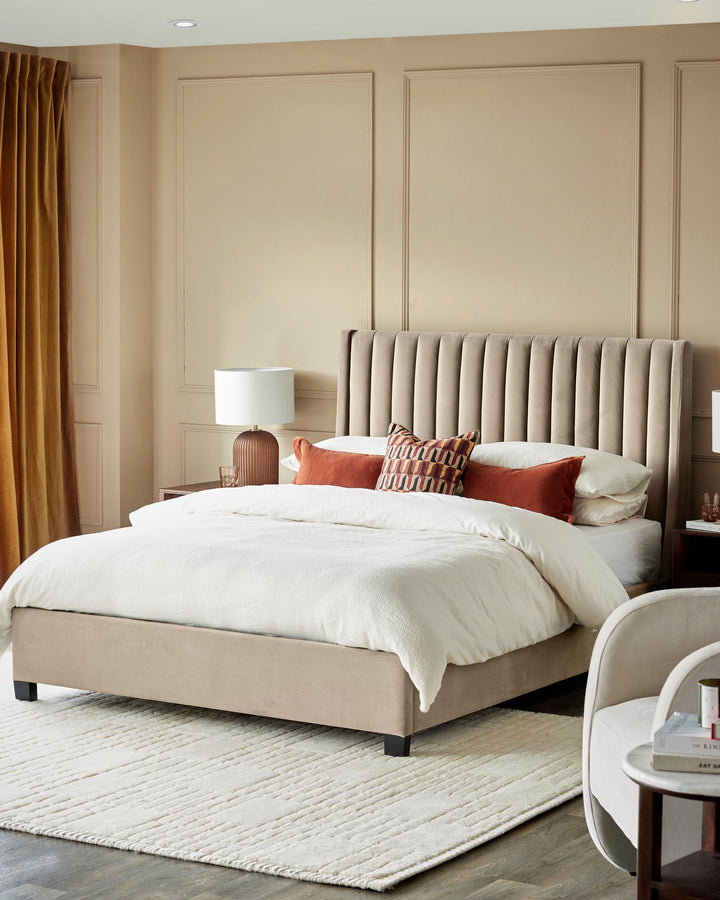 A neutral bedroom featuring a bed with a panelled headboard, a bedside table with a lamp, and a cream rug.
