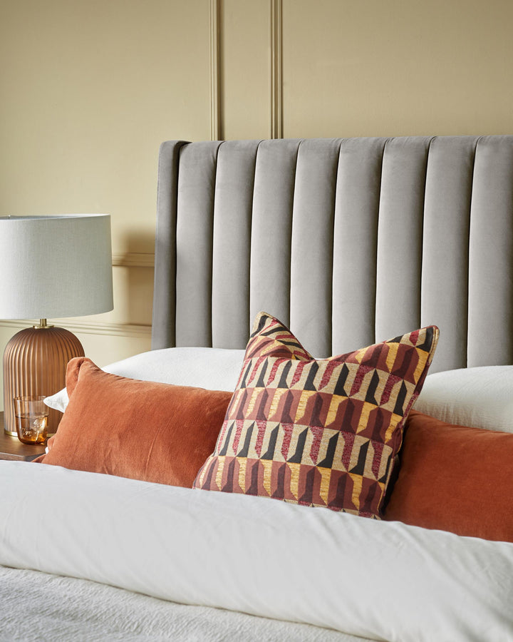 Bedroom featuring a grey headboard, lamp, and decorative cushions on a bed with white bedding.