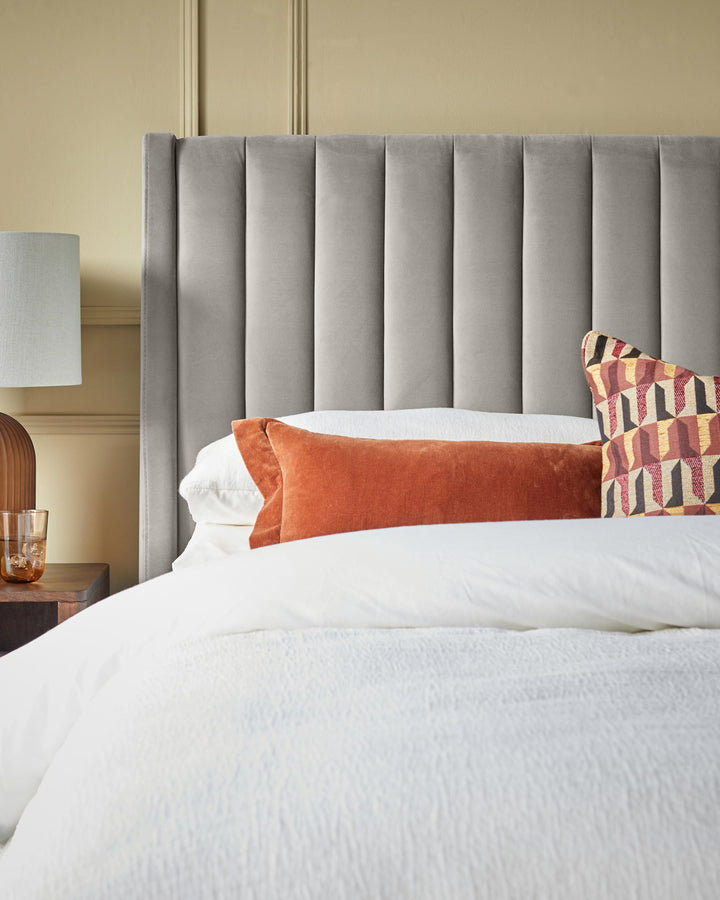 A modern bedroom featuring a grey headboard, a wooden bedside table and colourful decorative cushions.