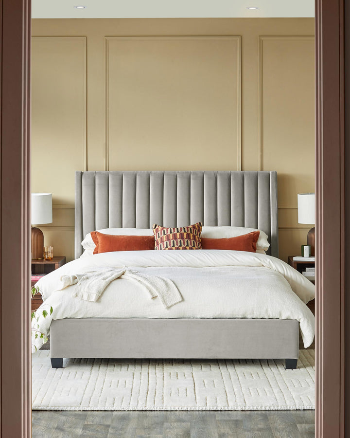 A grey upholstered bed and headboard, bedside tables and lamps displayed on a cream rug in a neutral bedroom.