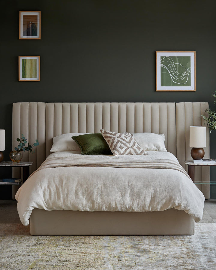 Bedroom with large, upholstered bed, two side tables with lamps and three framed prints on a dark green wall.