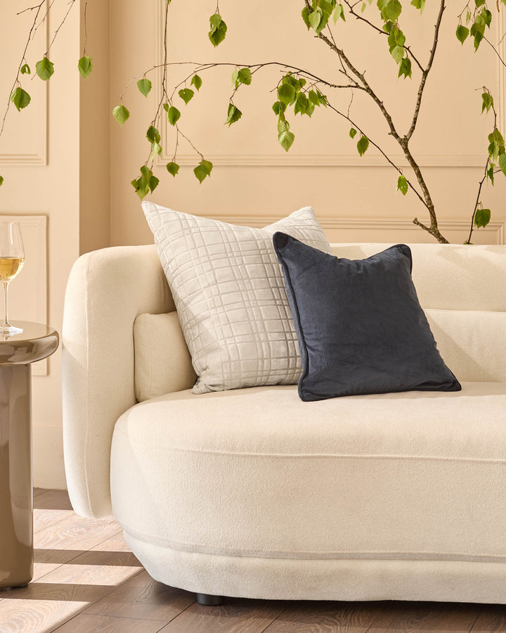 Arabella cushion in large ivory displayed on a cream curved sofa with decorative pillows.