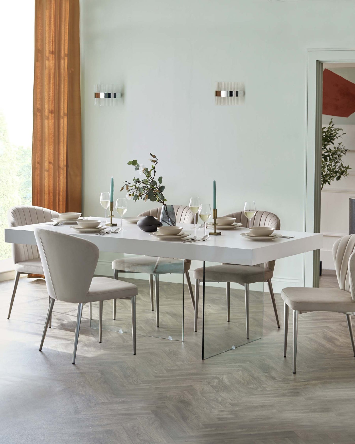 Modern dining room furniture set featuring a sleek white rectangular table with clear glass legs and six elegant upholstered chairs in a soft neutral tone, with subtle channel tufting and slim metal legs.