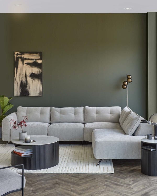 A modern gray sectional sofa, round black coffee table with marble top, and stylish side tables on a textured rug.