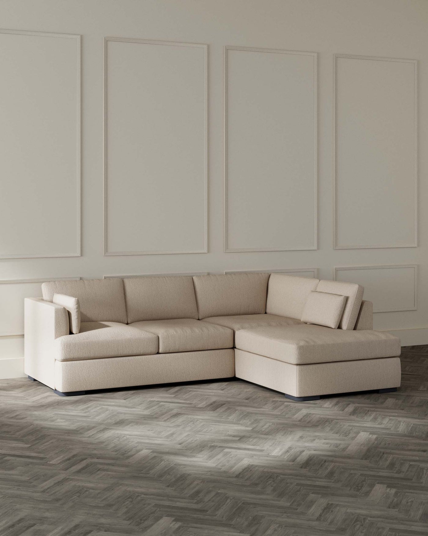 Contemporary L-shaped sectional sofa in a light beige textured fabric with a chaise lounge on the right side. The sofa has a low-profile design with clean lines, thick cushioned seating, and uniform backrests, elevated slightly off the floor with discreet dark legs. The setting is complemented by a herringbone hardwood floor and elegant panelled walls in a neutral tone.