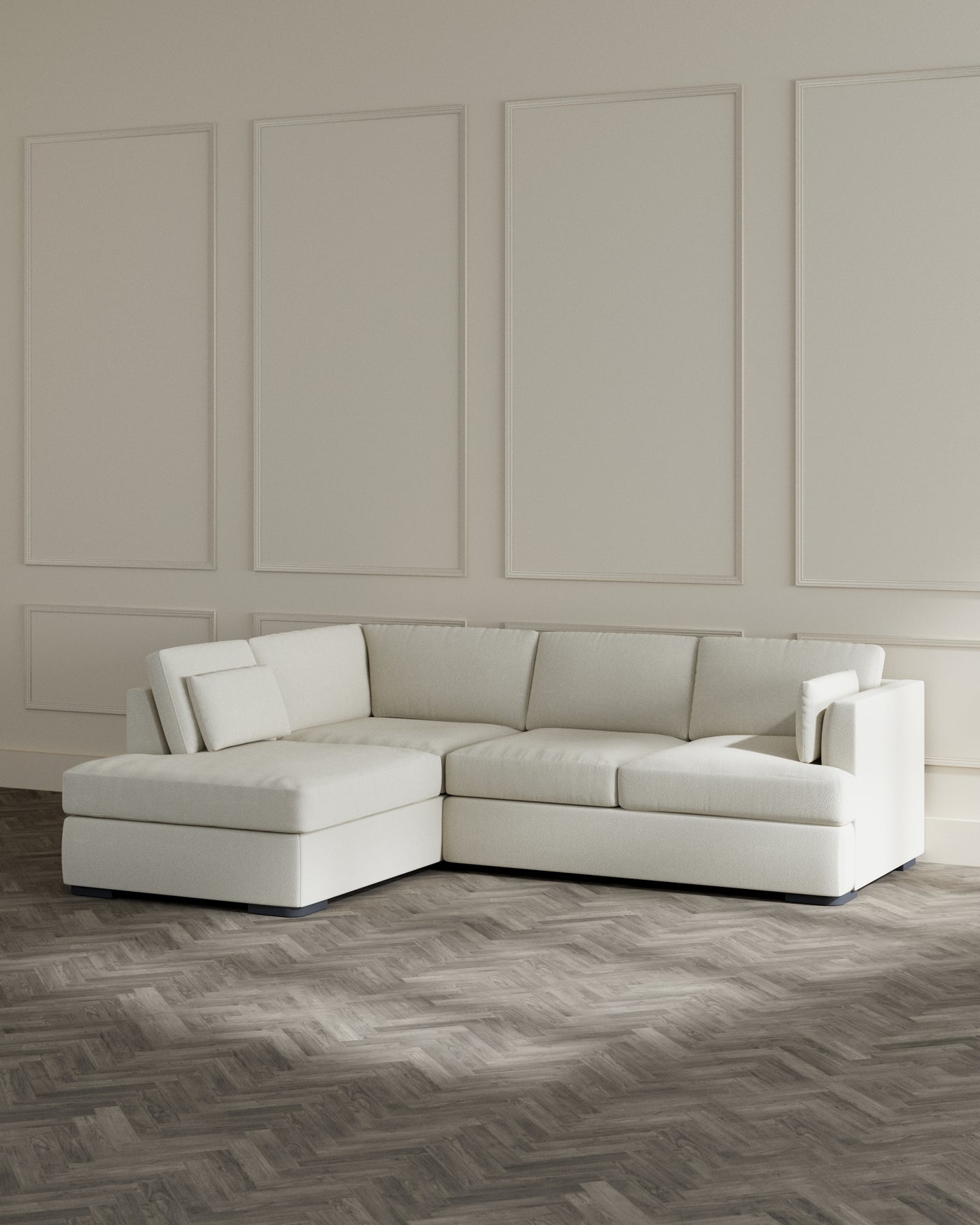 Modern L-shaped sectional sofa with a chaise lounge in a creamy white fabric, placed in a minimalist room with chic wall panelling and herringbone patterned wooden flooring.